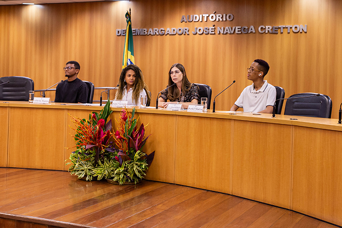 A imagem mostra uma terceira composição da mesa no Auditório Desembargador José Navega Cretton, dando continuidade ao mesmo evento anterior. Quatro pessoas estão sentadas atrás da mesa
